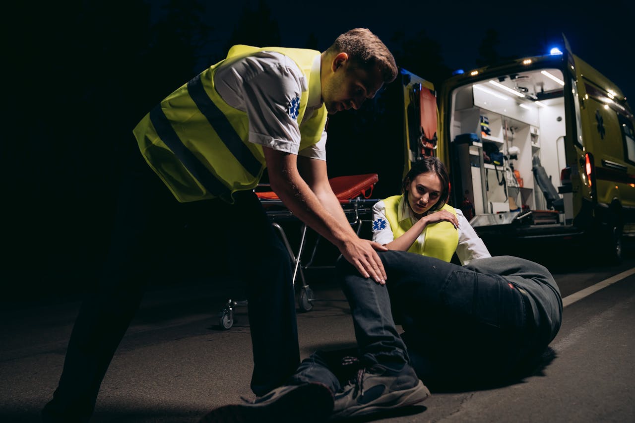 Paramedics providing first aid to a patient on road with ambulance in background.